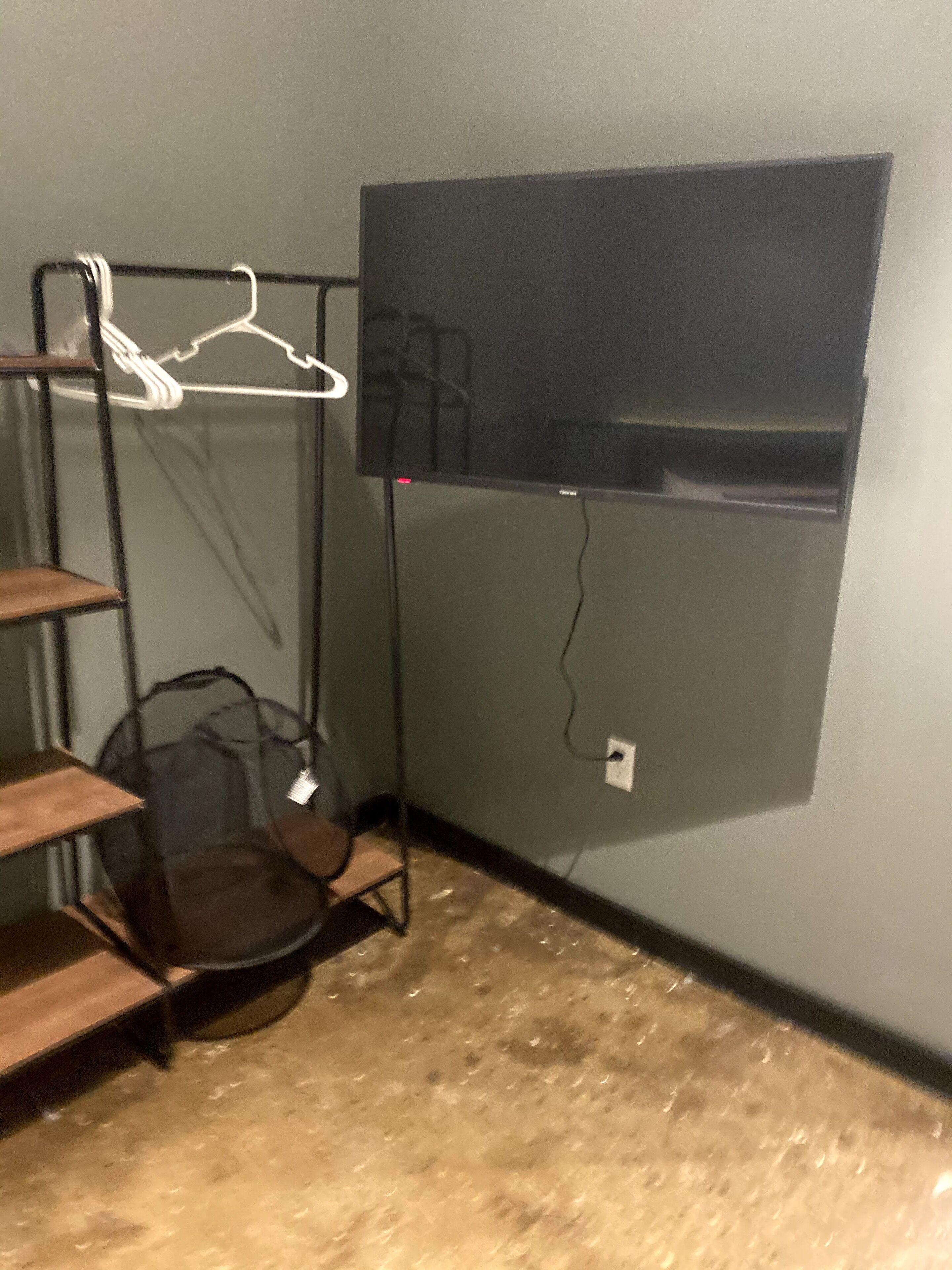 A room with a TV mounted on the wall, a metal shelf unit, and a wooden bench.