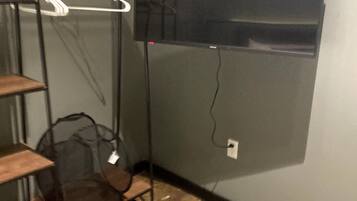 A room with a TV mounted on the wall, a metal shelf unit, and a wooden bench.