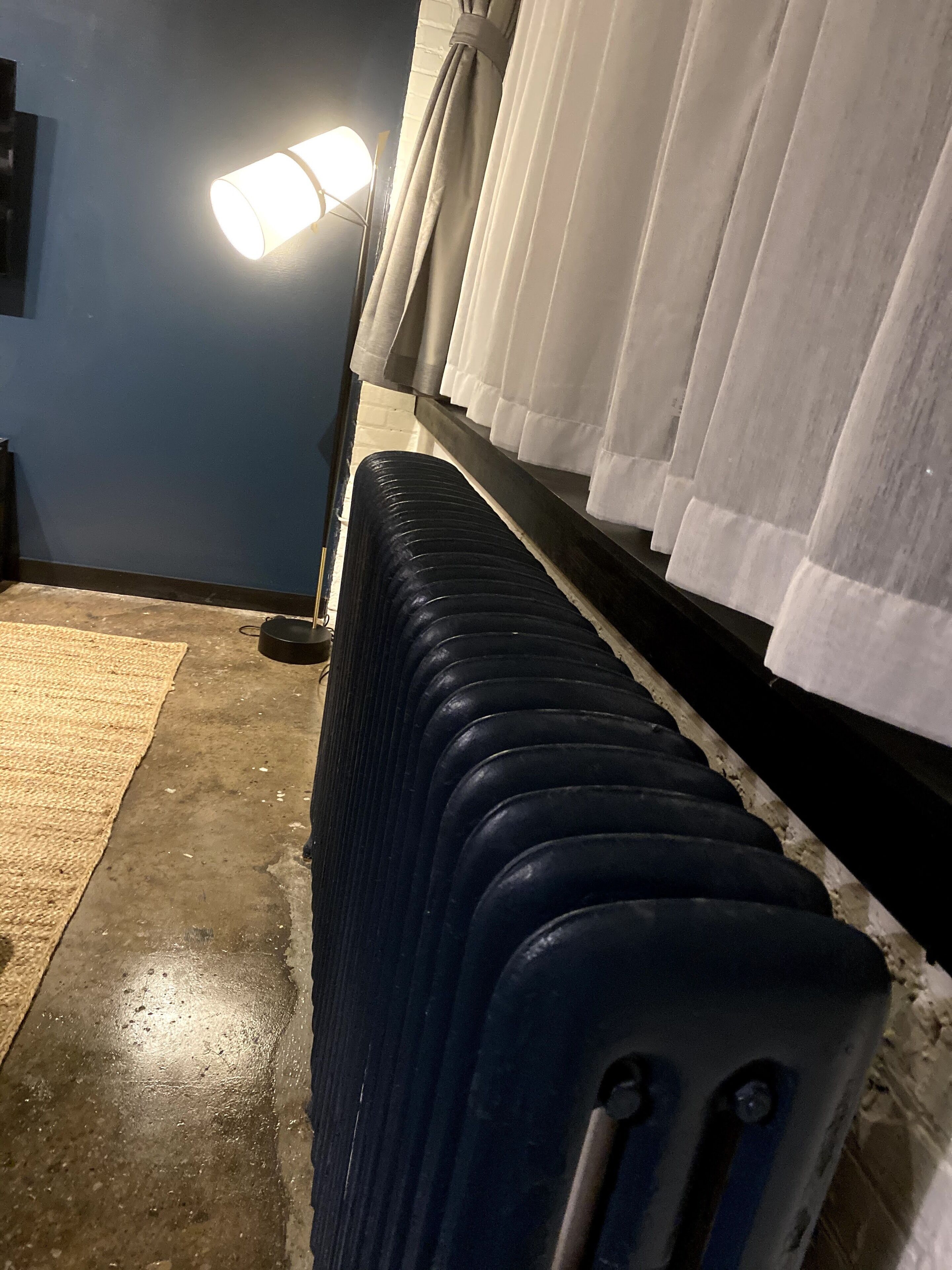 A row of stacked luggage against a wall with a floor lamp and curtains.
