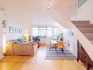 A modern living room with a sofa, TV, dining table, and chairs.
