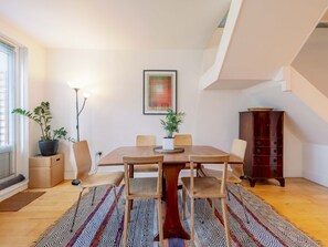 A dining area with a wooden table, four chairs, a floor lamp, and two potted plants.