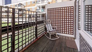 A balcony with a wicker chair, a wooden floor, and a view of neighboring buildings. - 3-Bedroom Duplex w/ Private Patio in Shoreditch - Pass the Keys (London)