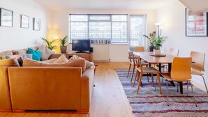 A modern living room with a sofa, TV, and dining area. - 3-Bedroom Duplex w/ Private Patio in Shoreditch - Pass the Keys (London)