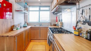 A modern kitchen with wooden cabinets, a gas stove, and a window providing natural light. - 3-Bedroom Duplex w/ Private Patio in Shoreditch - Pass the Keys (London)