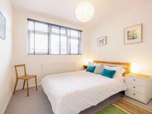 A bedroom with a large bed, a chair, a nightstand, and a window with blinds.