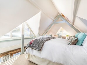 A bedroom with a sloped ceiling, large windows, a bed with pillows, and a radiator.