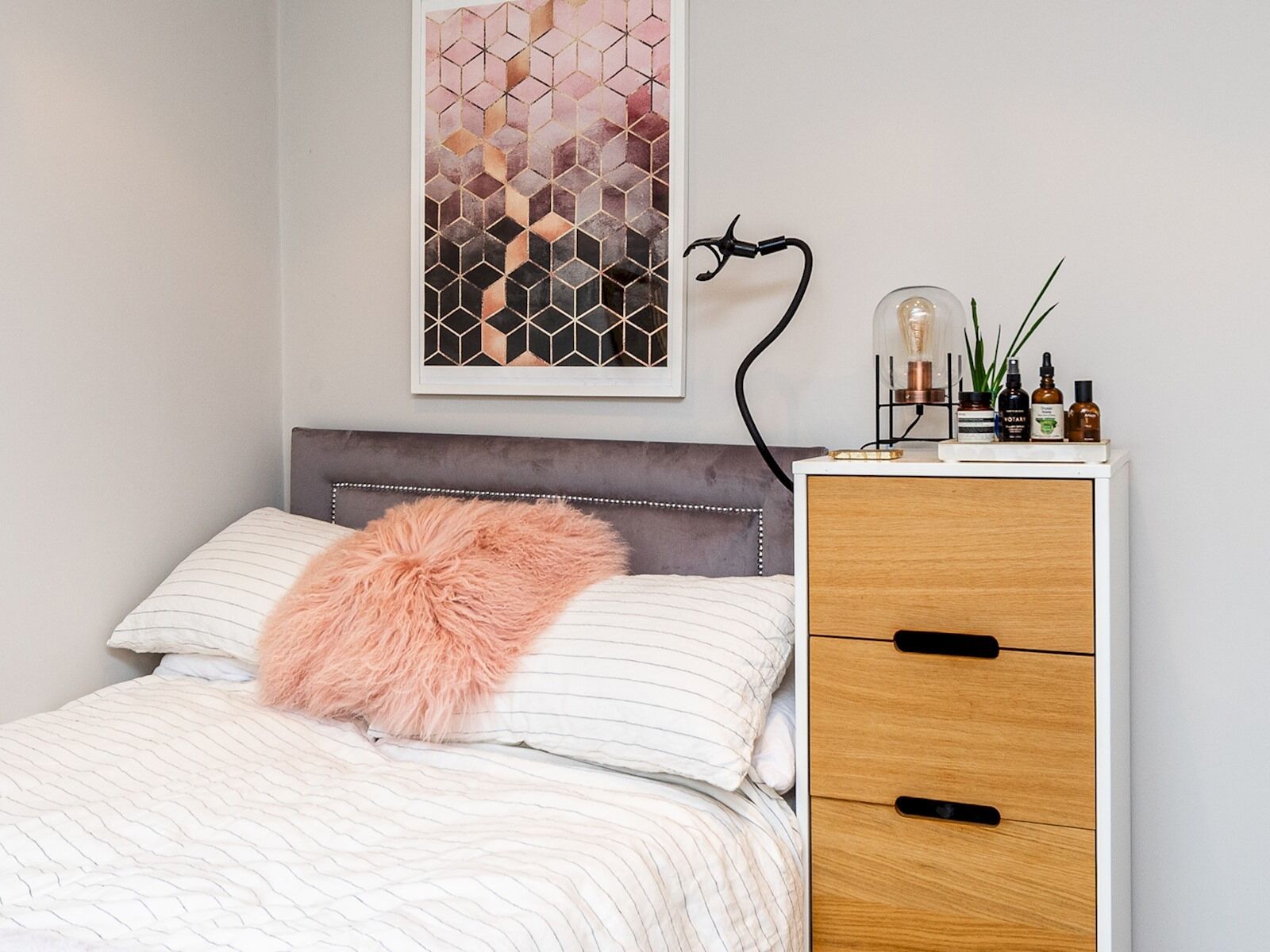A neatly arranged bedroom with a bed, a bedside table with a lamp, and a decorative wall piece.