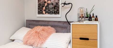 A neatly arranged bedroom with a bed, a bedside table with a lamp, and a decorative wall piece.
