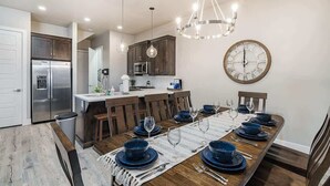 A dining area with a long wooden table set for six, surrounded by dark wooden chairs. A large wall clock is visible on the wall. - O-50&51 | 2 Homes! Pvt Heated Pool &  Pvt Hot Tubs (Santa Clara)