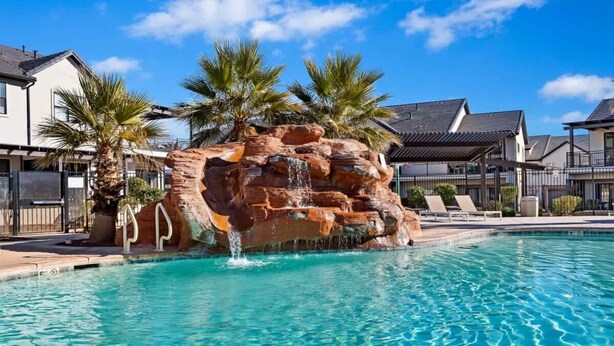 A swimming pool with a rock waterfall feature, surrounded by palm trees and modern houses. - O-50&51 | 2 Homes! Pvt Heated Pool &  Pvt Hot Tubs (Santa Clara)
