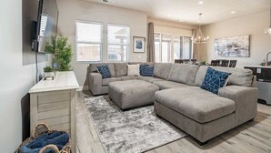 A modern living room with a sectional sofa, a flat-screen TV mounted on the wall, and a dining area with a chandelier. - O-50&51 | 2 Homes! Pvt Heated Pool &  Pvt Hot Tubs (Santa Clara)