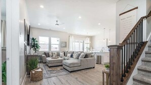 Una amplia sala de estar con un sofá modular grande, piso de madera y una escalera que conduce al piso superior.