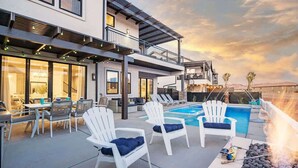 Un área de piscina moderna al aire libre con sillones de descanso, una parrilla y un porche cubierto.