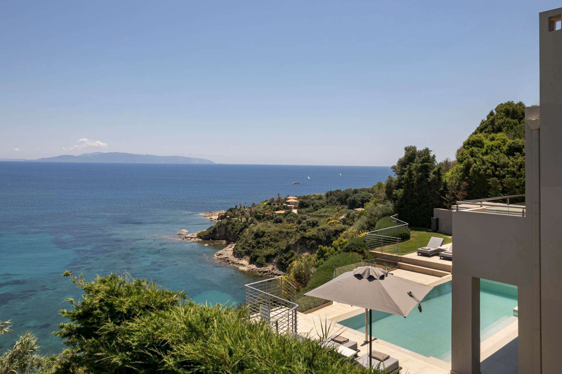 A pool with a view of the sea, a staircase, and a building with a balcony.