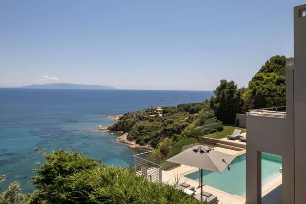 A pool with a view of the sea, a staircase, and a building with a balcony.