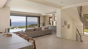 Ein modernes Wohnzimmer mit einer großen Couch, einem Esstisch und Meerblick.