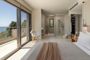 Ein modernes Schlafzimmer mit einem großen Bett, einem kleinen Sessel, einem begehbaren Kleiderschrank und einer Glasdusche.