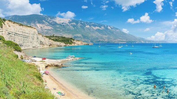 Ein Küstenstrand mit klarem türkisblauem Wasser, felsigen Klippen und Booten.