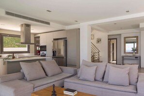 A modern living room with a grey sofa, a coffee table, and a kitchen area with a fridge and stove.