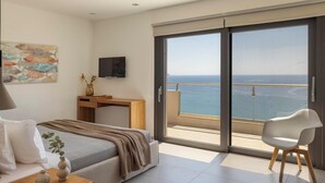 Ein modernes Schlafzimmer mit Bett, Schreibtisch, Fernseher und einem Balkon mit Meerblick.