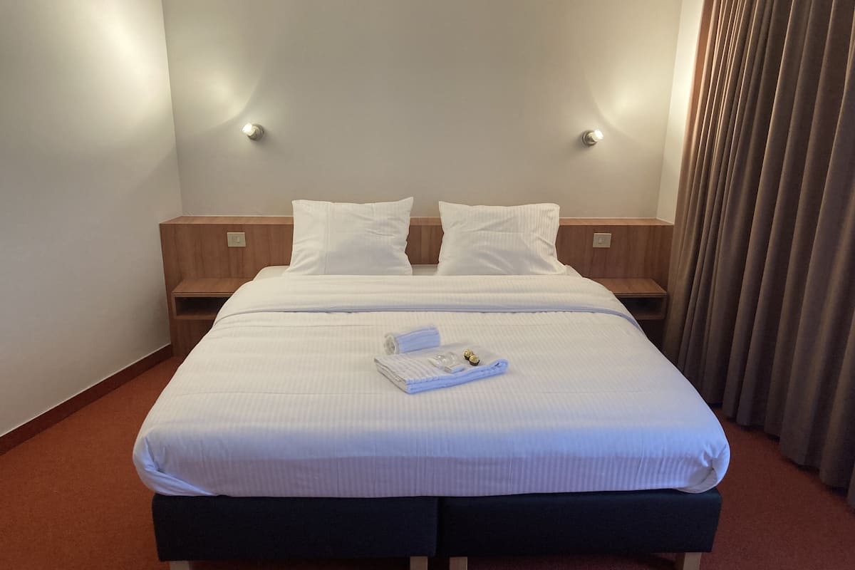A hotel room with a large bed, two bedside tables, and a curtain.