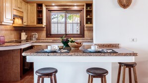 A kitchen with wooden cabinets, a granite countertop, a central island with stools, and a view through a glass door. - Panoramic views and ideal area to rest and see the island of La Palma (Villa de Mazo)