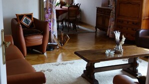 Una sala de estar con piso de madera, un sofá de cuero marrón, una mesa de centro y un comedor con mesa y sillas.