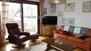 Una sala de estar con un sofá y un sillón de cuero marrón, una mesa de centro de madera y un televisor sobre un mueble de madera.