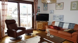 A living room with a brown leather sofa, a brown leather chair, a wooden coffee table, and a TV on a wooden stand.