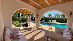 Un espace extérieur aménagé avec des sièges, protégé du soleil, et une piscine en arrière-plan.