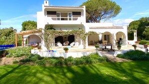 Un bâtiment blanc à deux étages, doté d’un patio couvert, d’un espace extérieur aménagé pour s’asseoir et d’une piscine.
