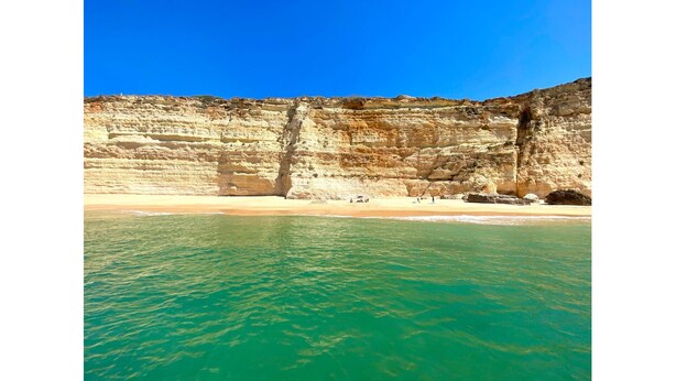 Une plage à l’eau turquoise et limpide, avec une falaise rocheuse en arrière-plan.