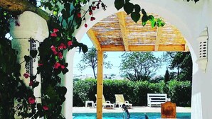 Un espace piscine extérieur agrémenté d’une pergola, de chaises longues et d’une table aménagée pour les repas.