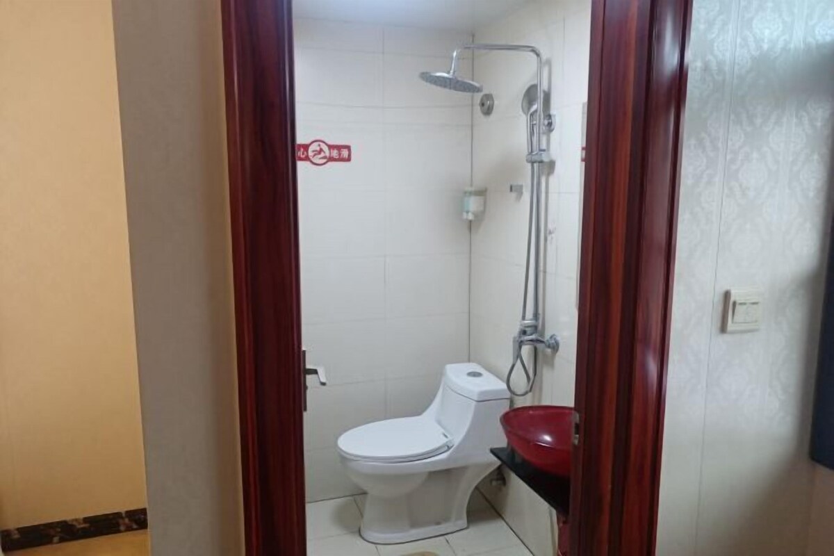 A small, private bathroom with a toilet, a shower, and a red basin.