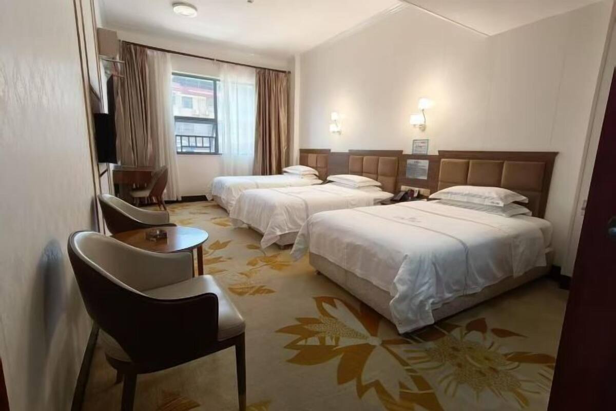 Habitación de hotel con dos camas, un escritorio, una silla y una ventana con cortinas.