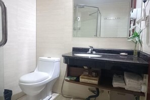 A bathroom with a white toilet, a black sink, a mirror, and a shower area. - Huayan Hotel (Yongzhou)