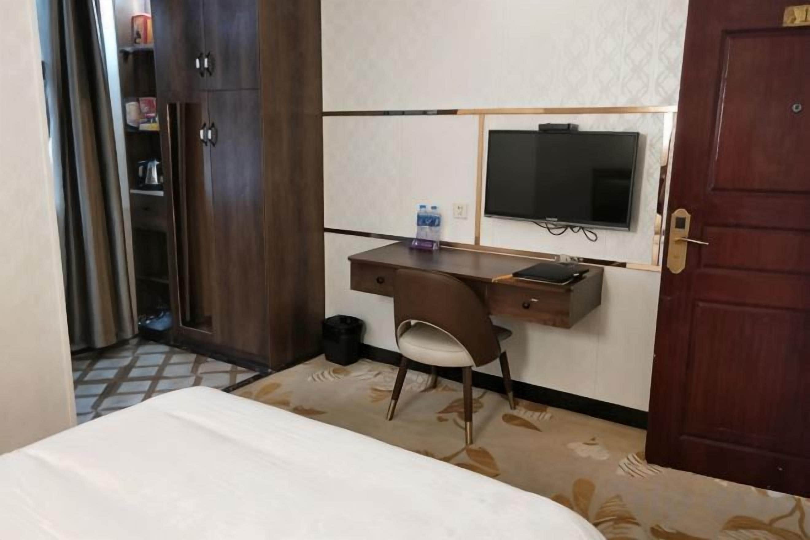 A hotel room with a bed, a desk with a chair, a television, and a wardrobe.