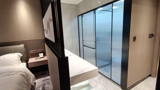 Une chambre d’hôtel moderne équipée d’un lit, d’une table de chevet, d’un téléphone et d’une porte d’ascenseur en verre.