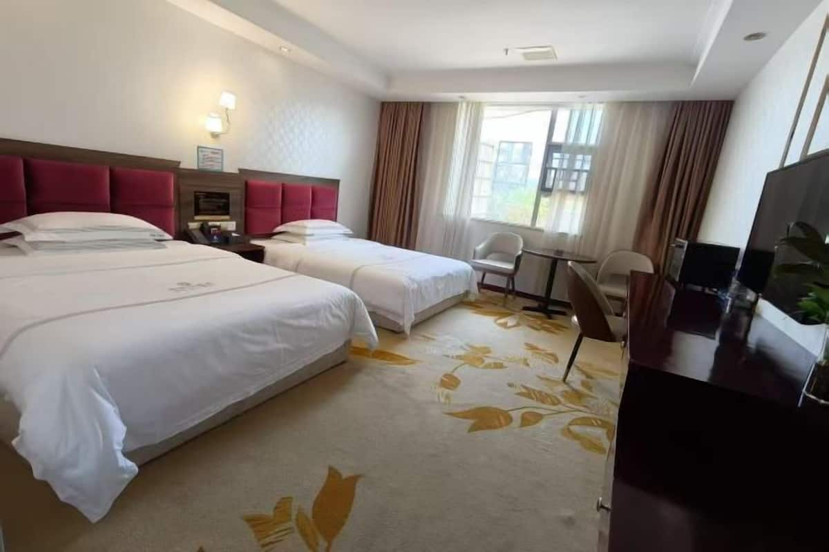 Habitación de hotel con dos camas, un escritorio, una silla, un televisor y una ventana con cortinas.