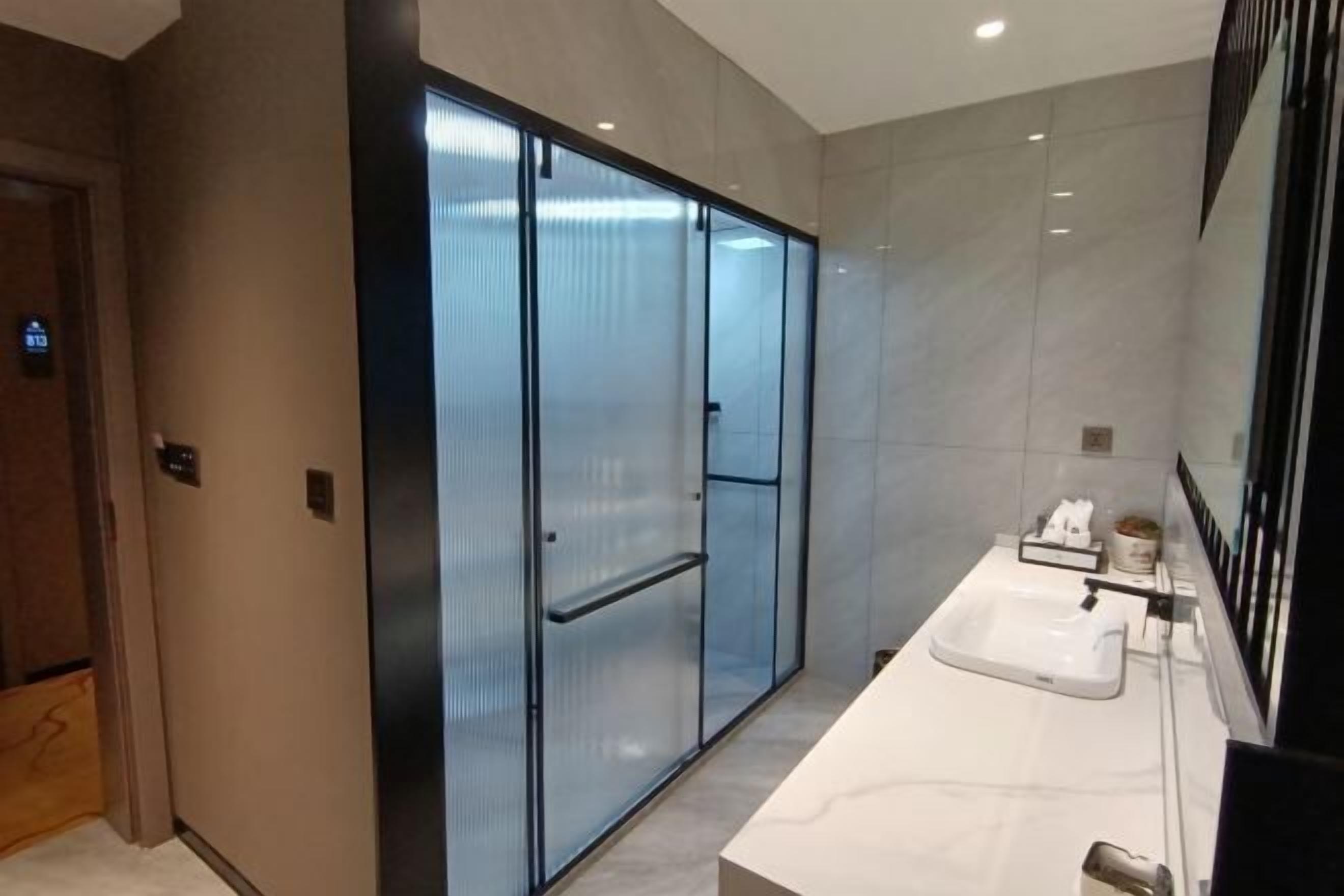 A modern bathroom with a large mirror, a white sink, and a glass-enclosed shower area.