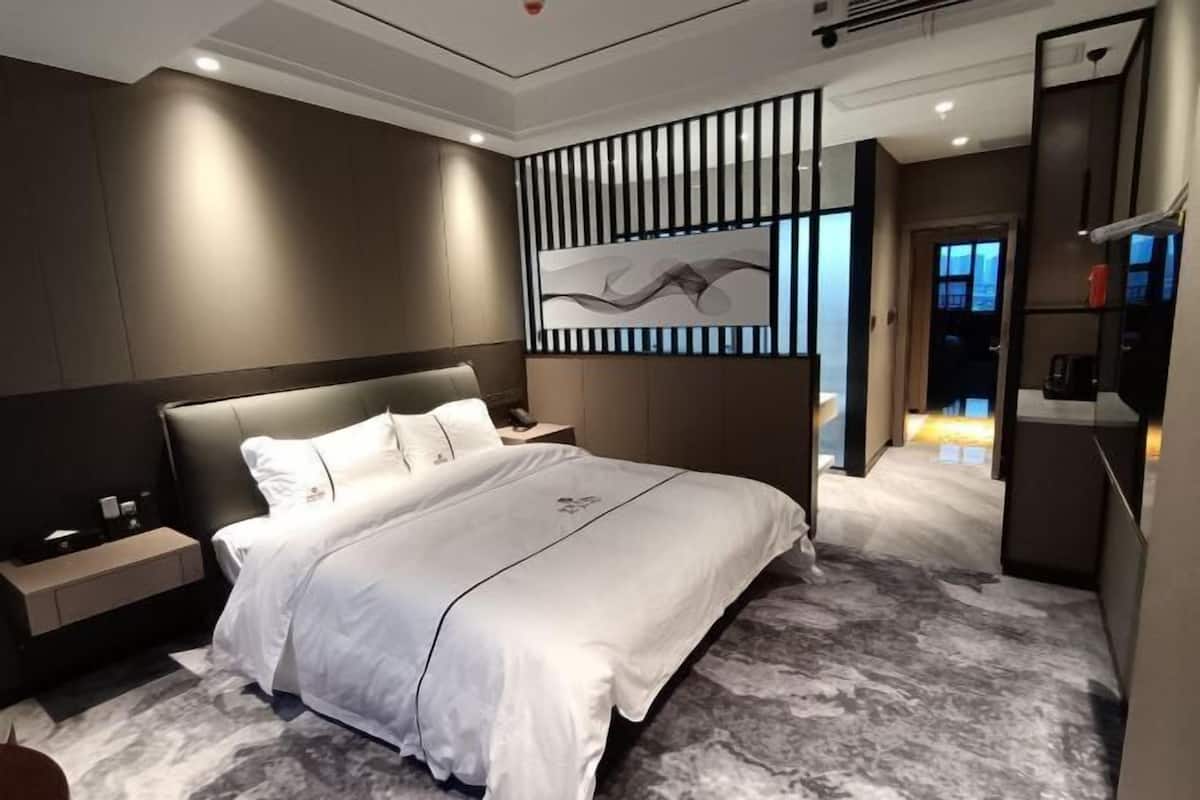 Una habitación de hotel moderna con una cama grande, una mesita de noche, un televisor montado en la pared y un panel decorativo.