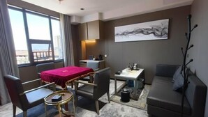 Une chambre d’hôtel équipée d’une table à manger, de deux chaises, d’un canapé, d’une petite table basse, d’une poubelle et d’une grande fenêtre avec des rideaux.