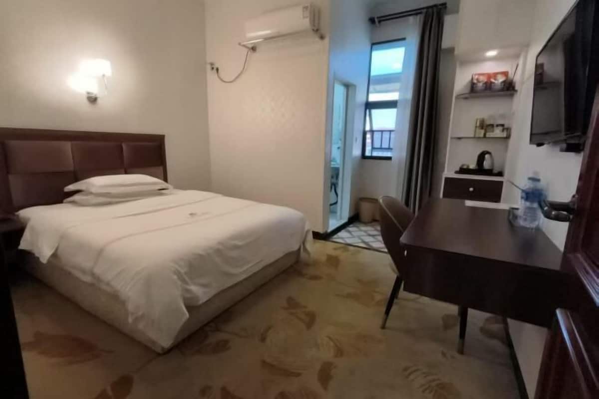 Habitación de hotel con cama, escritorio, silla, televisor y baño visible a través de una puerta abierta.