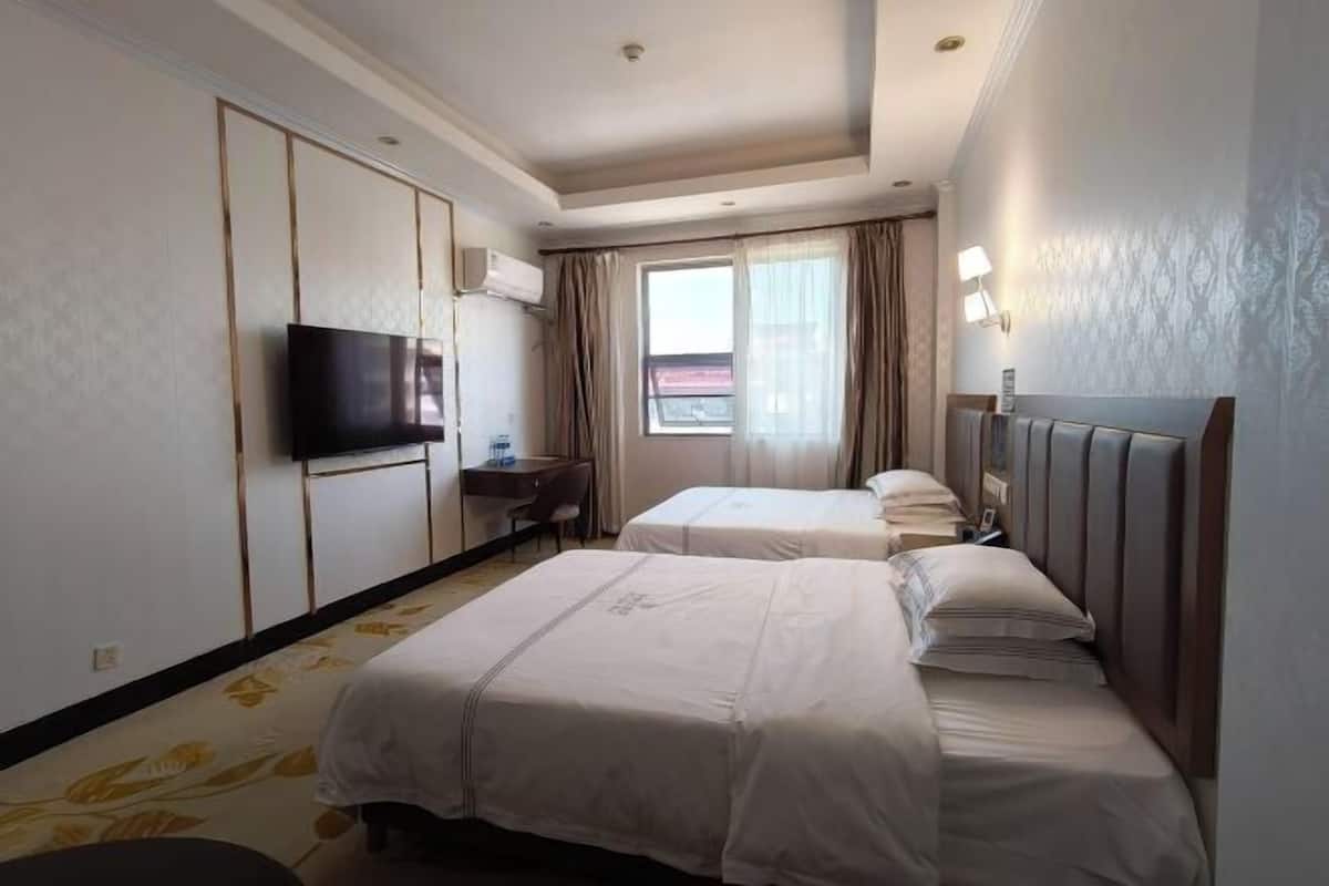 Habitación de hotel con dos camas, televisión, escritorio y ventana con cortinas.