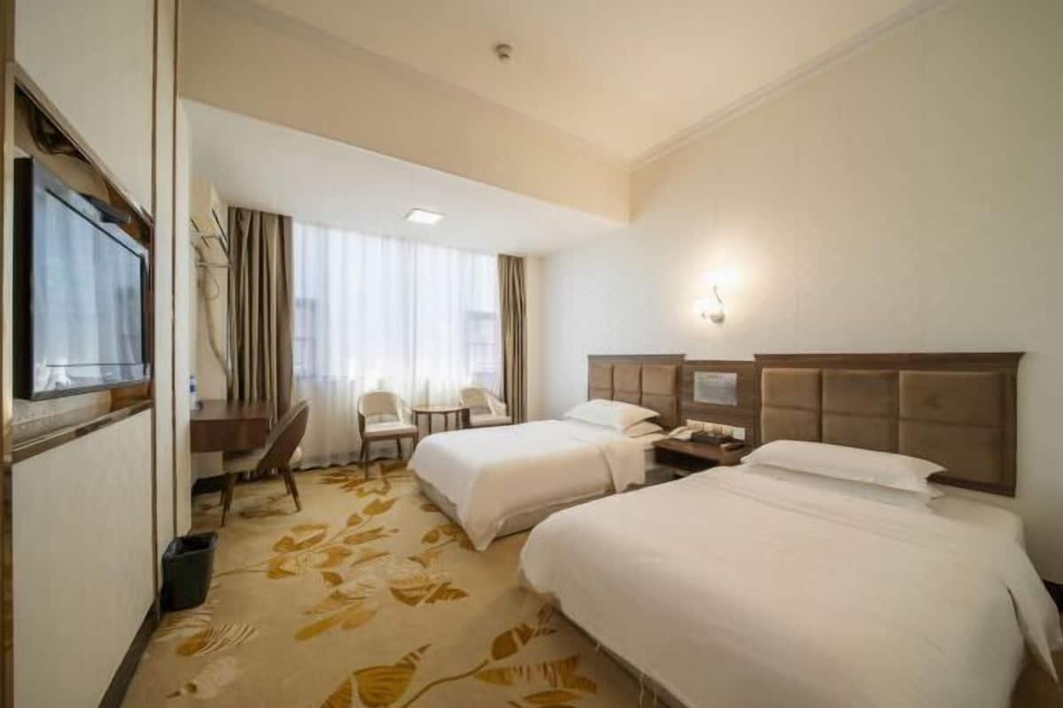 Una habitación de hotel con dos camas, un escritorio, una silla y un ventanal con cortinas.