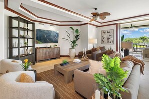 A modern living room with a fireplace, a large painting, and a view of the outdoors. - Kolea 1E - 3 BR Oceanview Vacation Rental - Hilton Waikoloa Access Included (Waikoloa)