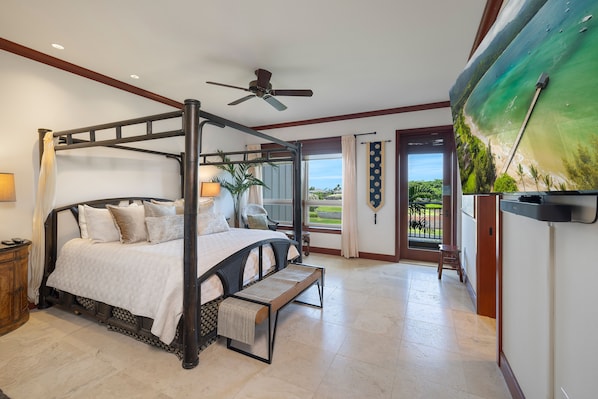 A four-poster bed with a bench, a ceiling fan, and a view of the ocean through a large window.