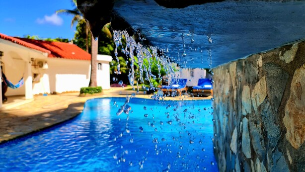 A swimming pool with clear water and visible bubbles, surrounded by a stone wall and a building with a red roof. - Exclusive Luxury Getaway: 6 BRM Tropical Villa, Just 5 Minutes from Beaches (Sosúa)
