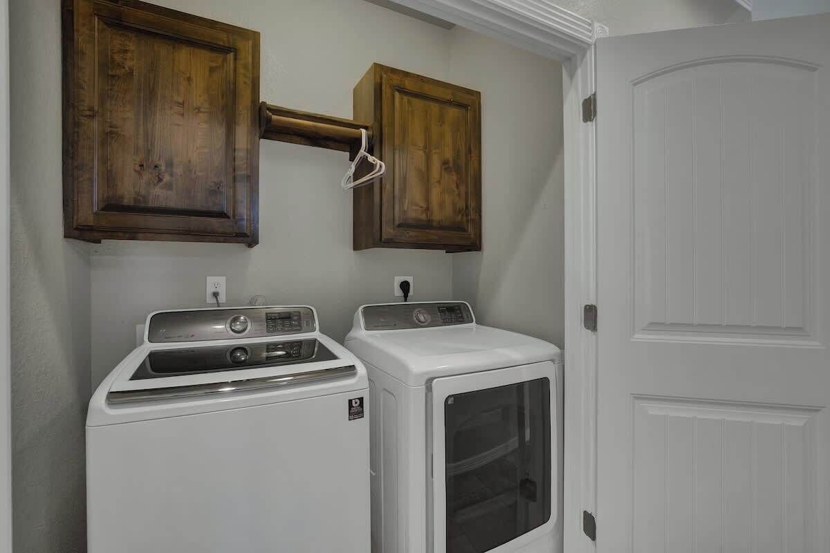 A laundry room with two white dryers and wooden cabinets above them.