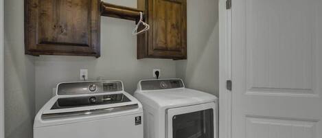 A laundry room with two white dryers and wooden cabinets above them.